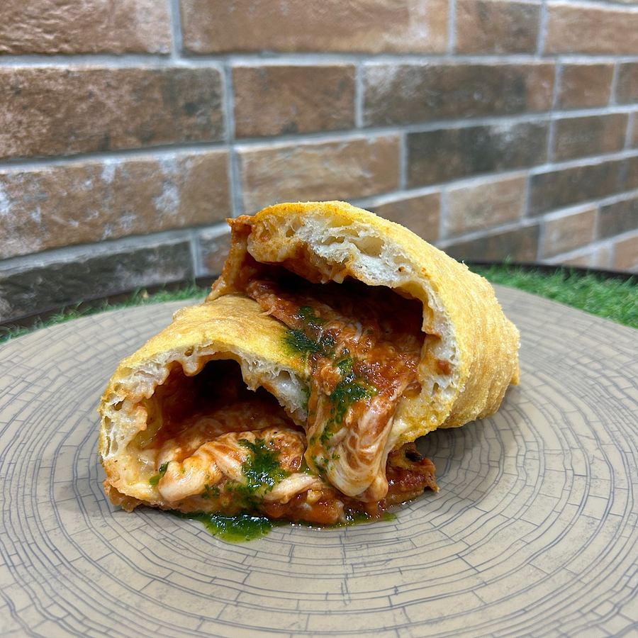 Un calzone fritto tagliato a metà con il ripieno filante, appoggiato su un piatto di legno.