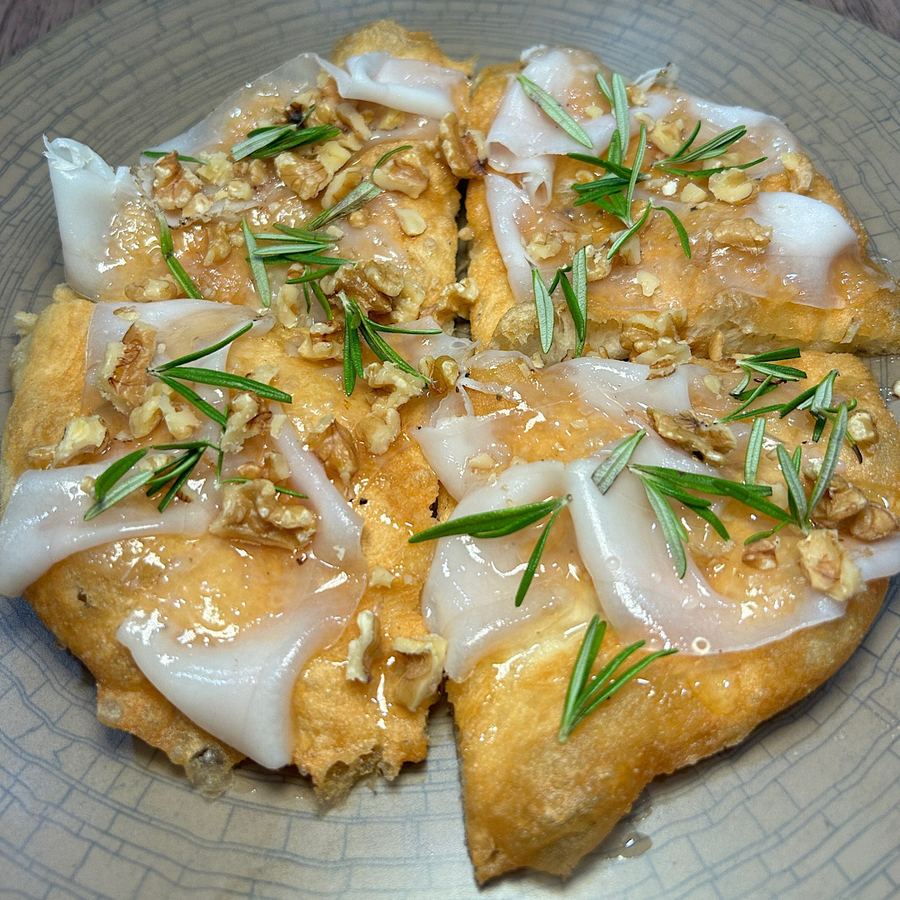 Pizza fritta aperta con lardo, noci, miele e rosmarino fresco, tagliata a spicchi.
