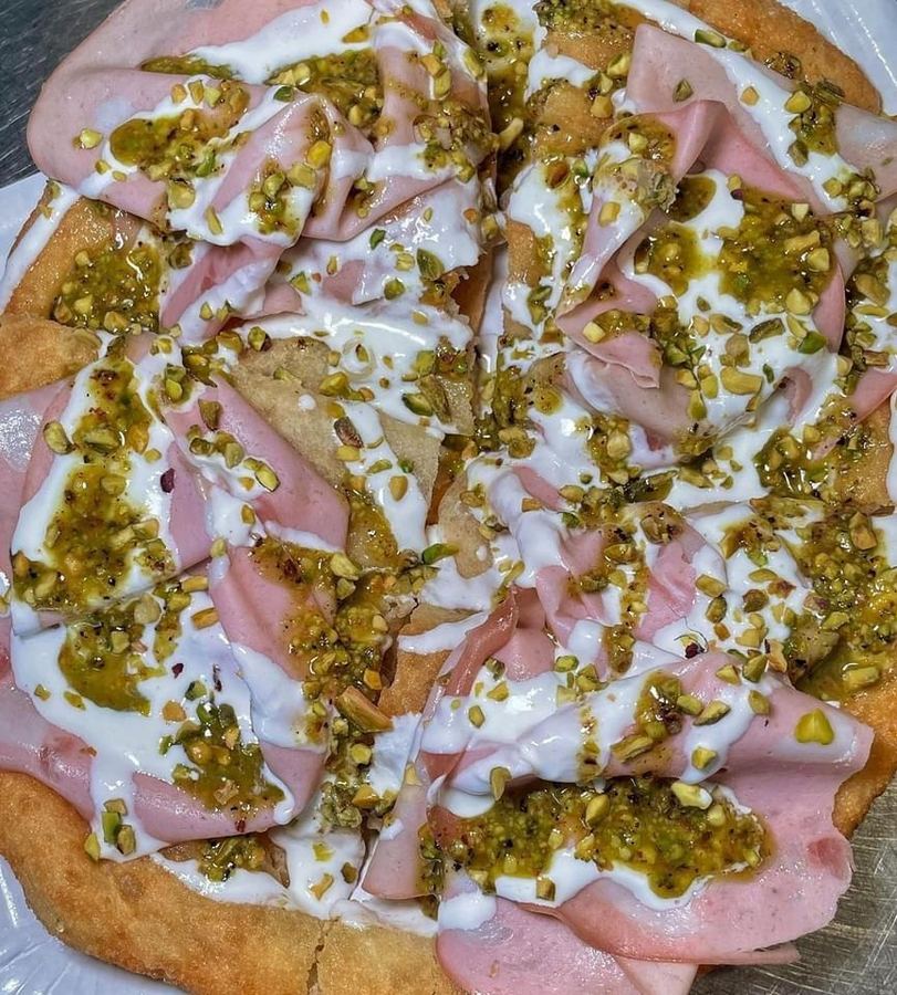 Pizza fritta aperta con mortadella a fette sottili, ciuffi di burrata e pesto di pistacchio.