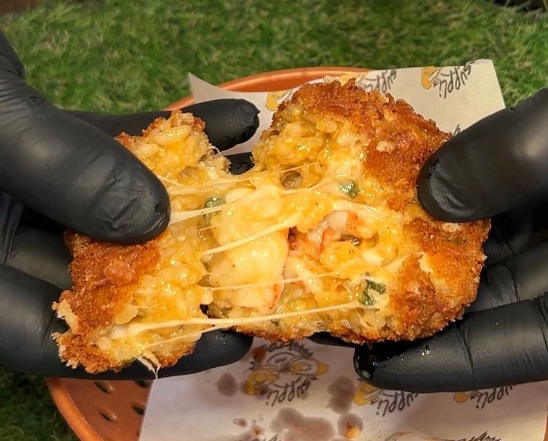 Un fritto appena spezzato a metà, tenuto con i guanti sopra la carta stampata del locale, con il ripieno filante ancora caldo.