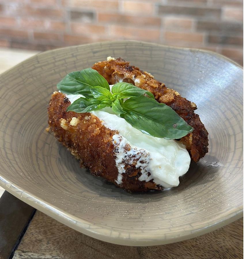 Un supplì aperto a metà con stracciatella fresca e una foglia di basilico, servito su un piatto scuro.