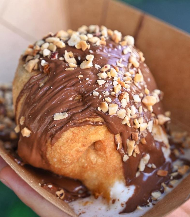 Dolce fritto ricoperto di crema alla nocciola e granella, servito in un vassoio di carta.
